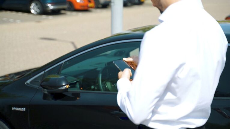 Medewerker opent een poolauto met haar smartphone bij een organisatie met meerdere voertuigen.